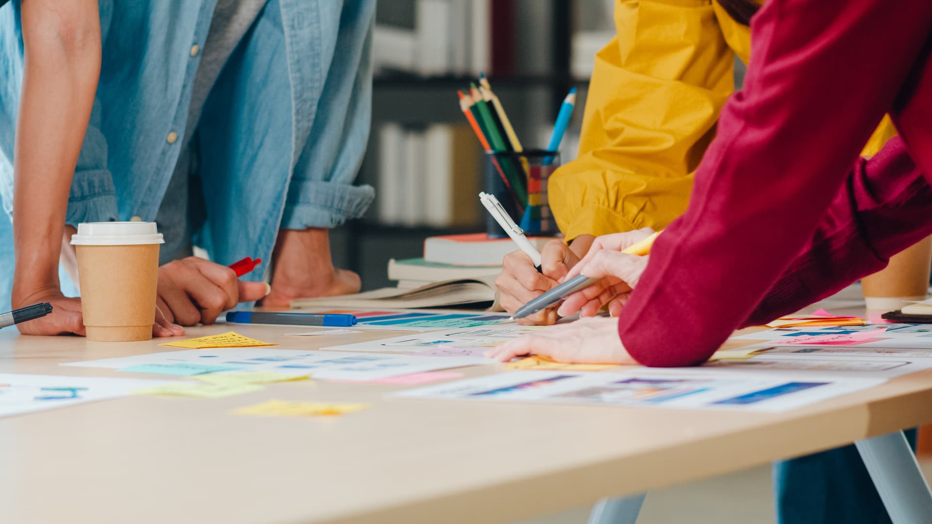 Three women in blue, yellow and red shirts designing a product